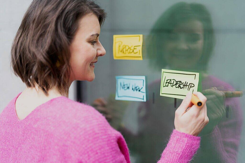 Teamentwicklung: Berlin, online & bundesweit - Zeit für euch, um mit Leichtigkeit und Erfolg zusammenzuarbeiten. Auf dem Bild ist Coach Romy Möller mit drei Post-its an einer Wand zu sehen.