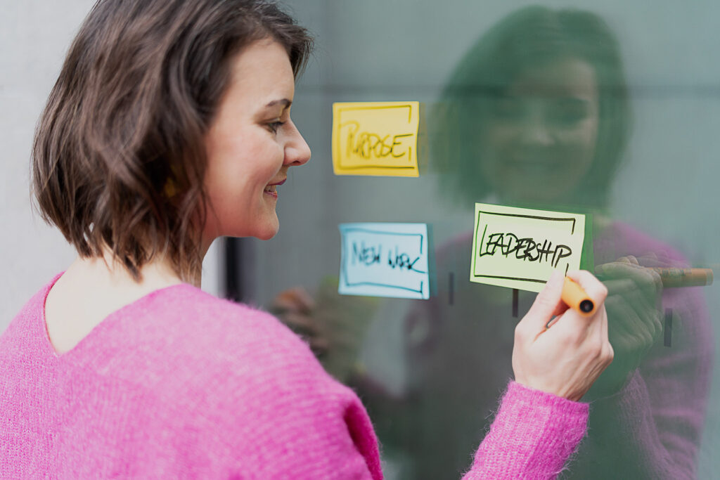 Teamentwicklung: München, online & bundesweit - Zeit für euch, um mit Leichtigkeit und Erfolg zusammenzuarbeiten. Auf dem Bild ist Coach Romy Möller mit drei Post-its an einer Wand zu sehen.