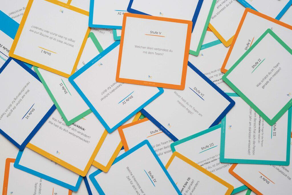 Check-In Fragen in Meetings: Startet mit einer gemeinsame Check-In Runde, damit alle im Team ankommen können. Auf dem Bild sind verschiedene Fragenkarten aus dem Teamkarten-Set zu sehen.