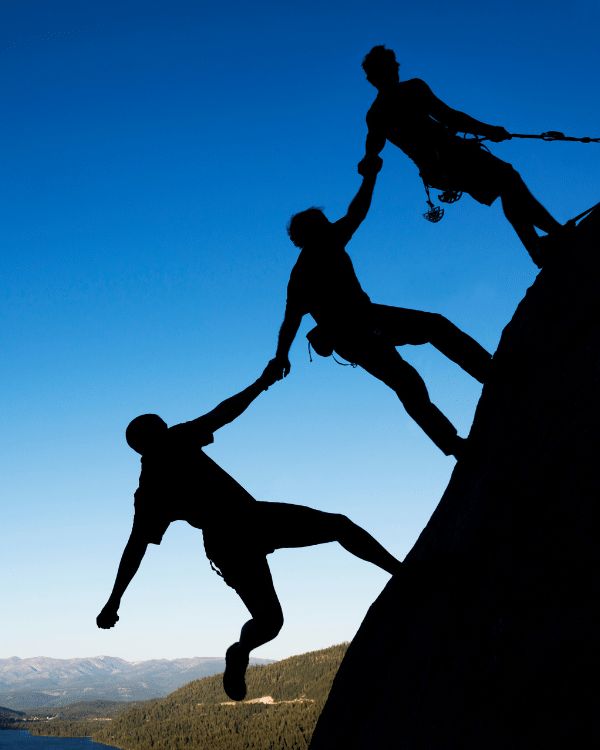 Team Zusammenhalt stärken: Die psychologische Sicherheit, der Umgang mit Unerwartetem, die Verarbeitung von Herausforderungen und das ganzheitliche Vorgehen sind Schlüssel für den Erfolg deines Teams in einer zunehmend unbeständigen Welt. Auf dem Foto sind drei Bergsteiger zu sehen, die sich an den Händen halten.